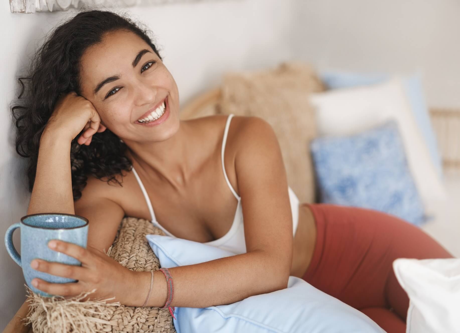 Smiling woman with dark hair reclining and holding a coffee cup